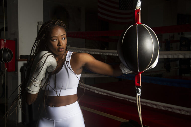 Young black woman training boxing in gym with the ring boxing ba
